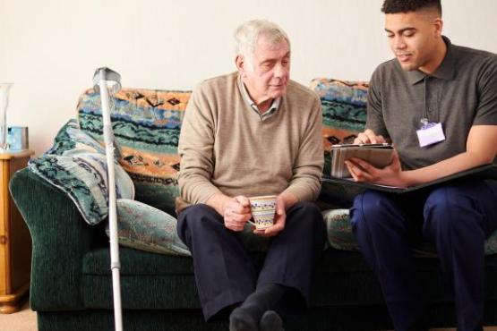 A senior man sitting with a care worker talking through treatment. 